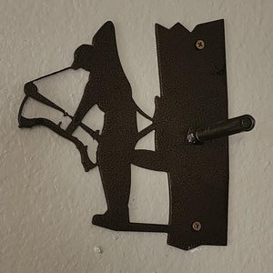 Puede incluir: Un soporte de pared de metal con forma de persona montando a caballo. El soporte está pintado de marrón y tiene un aspecto rústico. Está diseñado para sujetar un sombrero u otros objetos.