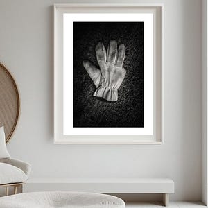 May include: A pair of work gloves in black and white, lying on a dark textured surface. The gloves are made of leather and have a worn look.