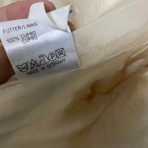 Może przedstawiać: Biała metka odzieżowa z tekstem "FUTTER/LINING 100% CUPRO CUPRO" i "MADE IN GERMANY". Metka zawiera r&oacute;wnież etykietę pielęgnacyjną z symbolami prania, prasowania i czyszczenia chemicznego.