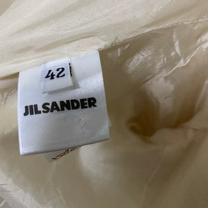 Może przedstawiać: Biała metka odzieżowa Jil Sander z nadrukowanym rozmiarem 42.