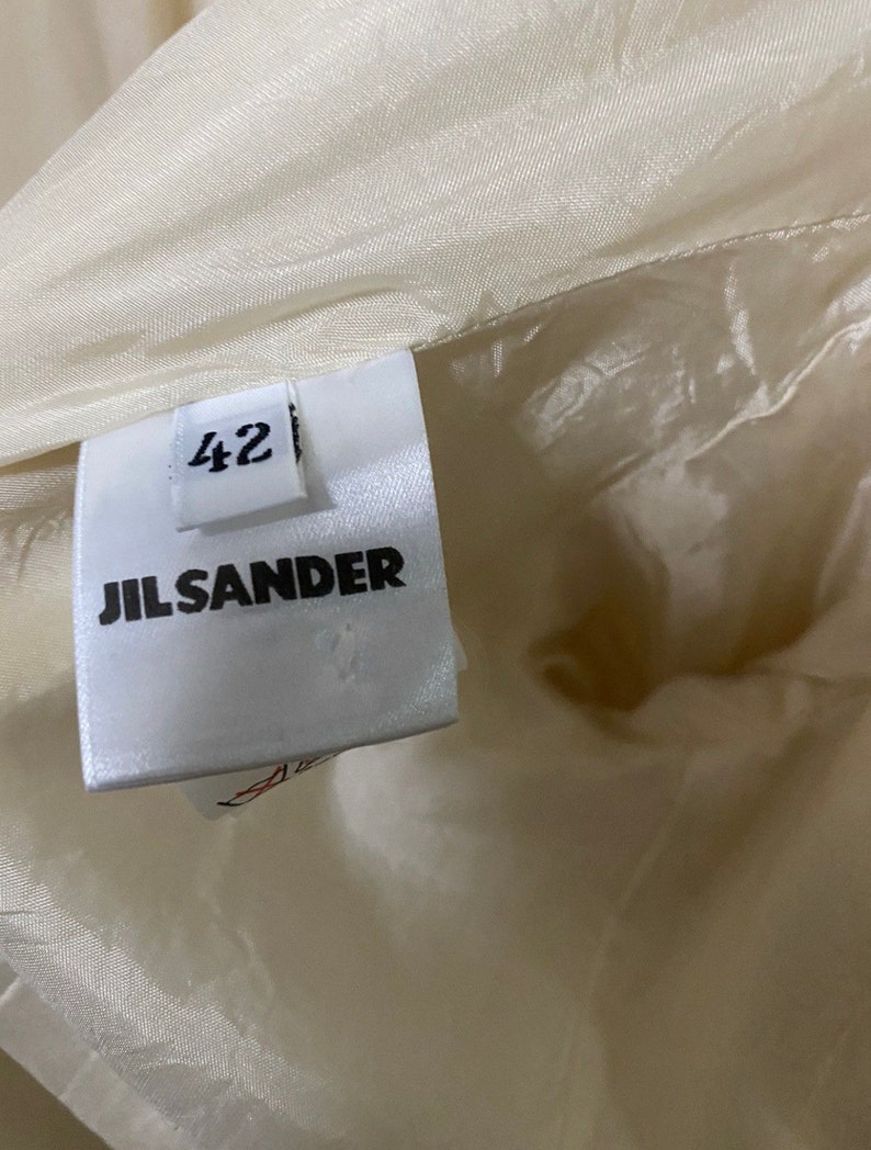 Może przedstawiać: Biała metka odzieżowa Jil Sander z nadrukowanym rozmiarem 42.