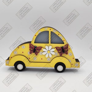 May include: A yellow wooden car with a white daisy and red butterfly design. The car is a decorative piece with a cutout for holding coasters.
