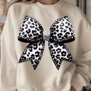 May include: A cream-colored sweatshirt with a large black and white leopard print bow with rhinestones.