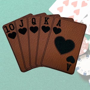 May include: A set of six playing cards, all hearts, including the 10, Jack, Queen, King, and two Aces. The cards are brown with black hearts and lettering.