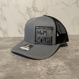 May include: Gray trucker hat with a black mesh back. The front patch features a slot machine graphic with the text "WEEKEND FORECAST 100% CHANCE OF PLAYING THE SLOTS."