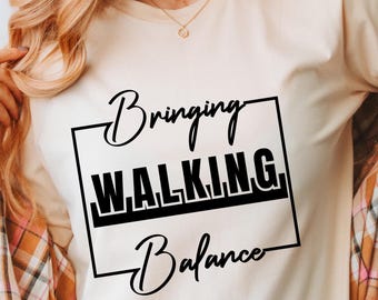 May include: A soft cream-colored t-shirt with the words "Bringing WALKING Balance" in black script and block letters. The shirt is paired with a plaid button-down shirt and blue jeans. The words "Soft Cream" and "In Pursuit of Style" are also visible.