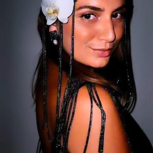 May include: A black beaded headpiece featuring a fine mesh net design with long, dangling beaded strands. The accessory is adorned with a single white orchid flower on the side and is paired with a matching black beaded earring with a white pearl.
