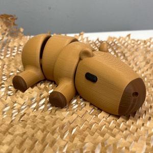 Puede incluir: Un juguete de madera de capibara marrón con un cuerpo segmentado, acostado sobre un fondo de papel marrón.
