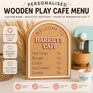 Puede incluir: Un letrero de men&uacute; de cafeter&iacute;a de juguete en madera con forma de arco que presenta el texto WELCOME TO HARRIET'S CAFE en letras rosas en relieve. La tabla enumera alimentos como Hot Dogs, Burger, Chips, Ice Cream y Drinks con sus precios.