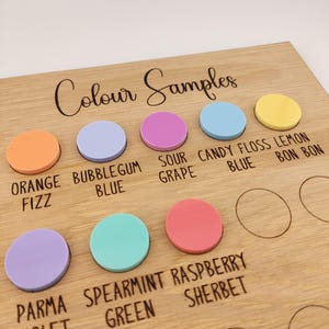 Puede incluir: Una tabla de madera etiquetada como Colour Samples con inserciones circulares de acr&iacute;lico en naranja, azul chicle, uva &aacute;cida, azul algod&oacute;n de az&uacute;car, lim&oacute;n, violeta parma, verde menta y frambuesa, con c&iacute;rculos vac&iacute;os para m&aacute;s muestras.