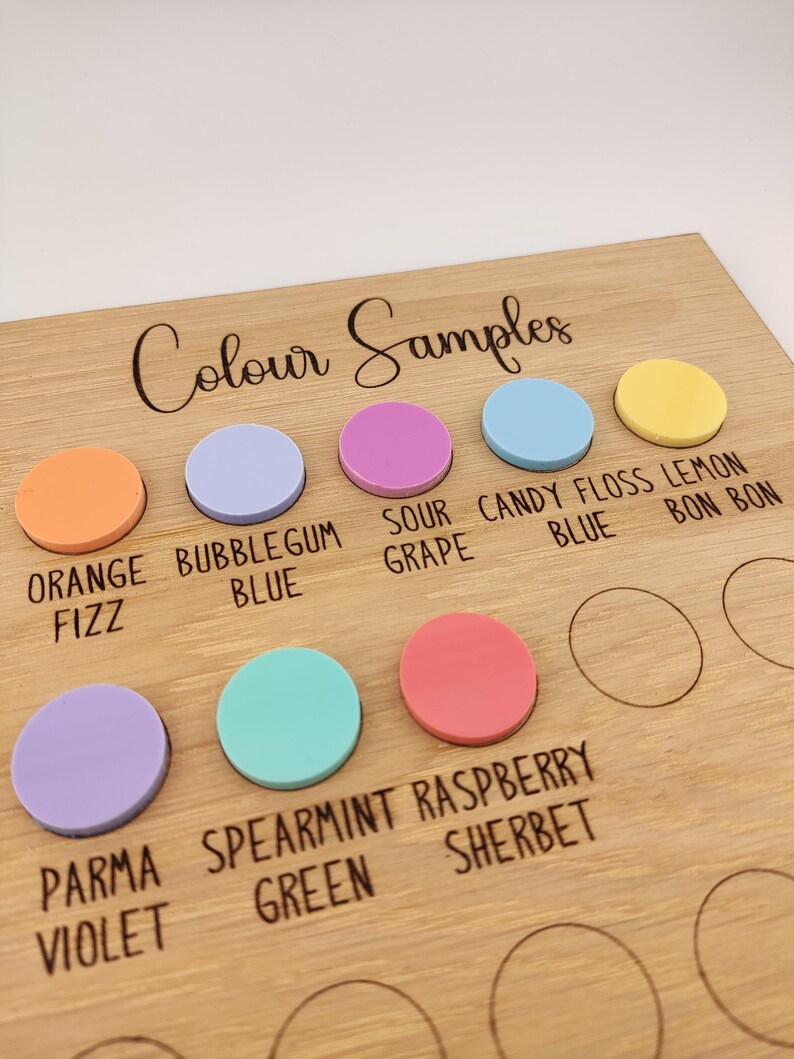Puede incluir: Una tabla de madera etiquetada como Colour Samples con inserciones circulares de acr&iacute;lico en naranja, azul chicle, uva &aacute;cida, azul algod&oacute;n de az&uacute;car, lim&oacute;n, violeta parma, verde menta y frambuesa, con c&iacute;rculos vac&iacute;os para m&aacute;s muestras.