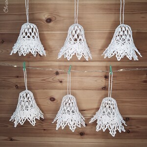 May include: Six white crocheted bells hanging from a string with green clothespins on a wood background. The bells are decorated with a lacy pattern. The text "Vintage Lady" is at the bottom of the image.