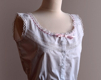 May include: White cotton camisole with a pink ribbon and lace trim. The camisole has a button closure in the front and a gathered elastic waistband.