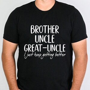 May include: Black t-shirt with white text that reads "BROTHER UNCLE GREAT-UNCLE I just keep getting better." The shirt is short-sleeved and appears to be made of a soft material. The text is in a bold, sans-serif font.
