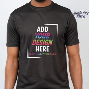 May include: Black short-sleeved t-shirt with the text "ADD YOUR DESIGN HERE" in a white frame, with the words in a rainbow gradient. The words "TEXT/IMAGE/PHOTO/LOGO" are below. The words "QUICK-DRY FABRIC" are in the upper right corner.
