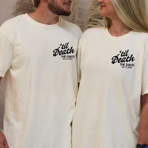 May include: Two cream-colored t-shirts with the phrase "'til Death" in a script font, along with "THE DAVIS 05.19.2025" printed in black. The shirts are worn by a couple, suggesting a matching set for a wedding or anniversary.
