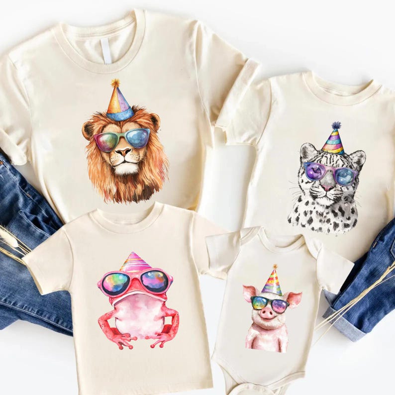 May include: A collection of cream-colored t-shirts and a baby bodysuit featuring watercolor illustrations of a lion, a leopard, a frog, and a pig. Each animal wears a colorful striped party hat and vibrant, multi-colored sunglasses.