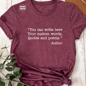 May include: A maroon t-shirt with the text "You can write here Your custom words, Quotes and poems." and "-Author" in white. The shirt has short sleeves and a round neckline. The tag on the shirt says "Heather Maroon".