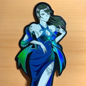 May include: A holographic sticker featuring a woman with long dark hair wearing a blue dress with a mermaid tail. The woman has a tattoo of an anchor on her arm and a heart on her leg. The sticker has a black background and iridescent blue and green accents.