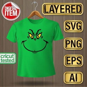May include: A green t-shirt with a black and yellow Grinch face graphic. The shirt is on a hanger and there are gold buttons with the words "LAYERED", "SVG", "PNG", "EPS", and "AI" on them.