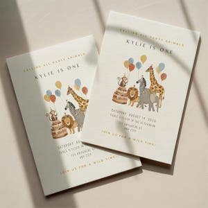 Op de afbeelding: Twee crèmekleurige uitnodigingen voor een feestje met gouden tekst en aquarel illustraties. De uitnodigingen luiden "Calling All Party Animals, Kylie is One". De illustraties bevatten een aap, een leeuw, een zebra, een giraf en een olifant. Ballonnen en een taart zijn ook aanwezig.