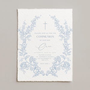 May include: A light blue floral wreath frames the text on a white invitation. The invitation reads "Please join us for the Communion of our son Owen" with event details. The paper has a textured, deckled edge.