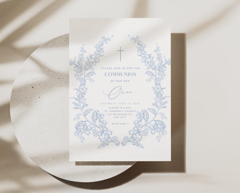 May include: A cream-colored invitation with blue floral wreath and cross design. The text reads "PLEASE JOIN US FOR THE COMMUNION OF OUR SON" with event details. The invitation is on a light gray surface.