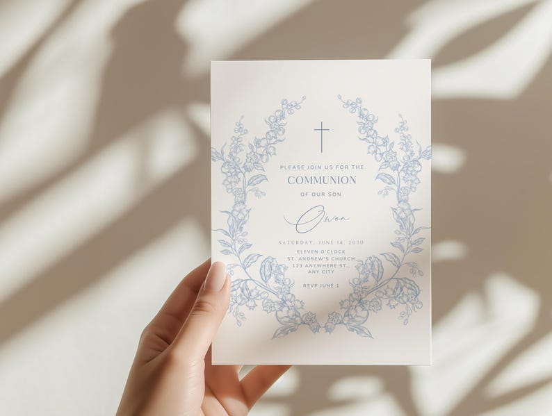 May include: A cream-colored invitation card with a blue floral wreath design and a cross at the top. The text reads "Please join us for the Communion of our son" with event details. The card is held by a hand.
