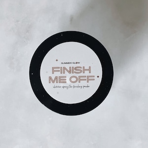 Pode incluir: Um adesivo redondo preto e branco com o texto "SUMMER GLOW FINISH ME OFF" e as palavras "shimmer spray tan finishing powder" em um tipo de letra menor.