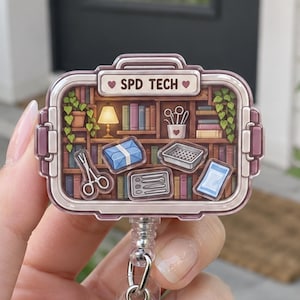 May include: A rectangular badge reel featuring a printed illustration of a bookshelf with medical instruments and the text SPD TECH. The design includes a small lamp, potted plants, surgical scissors, a tray, and various tools on wooden shelves.