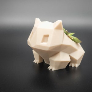 Peut inclure: Un pot de fleurs beige de forme géométrique en forme d'animal de dessin animé, avec une petite plante succulente qui pousse à l'intérieur.