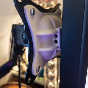 May include: A white plastic monitor mount with black metal accents. The mount is attached to a black metal pole.