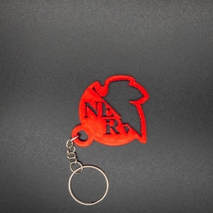 May include: A red plastic keychain shaped like a stylised heart with the word "NERV" printed on it. The keychain has a silver metal ring.