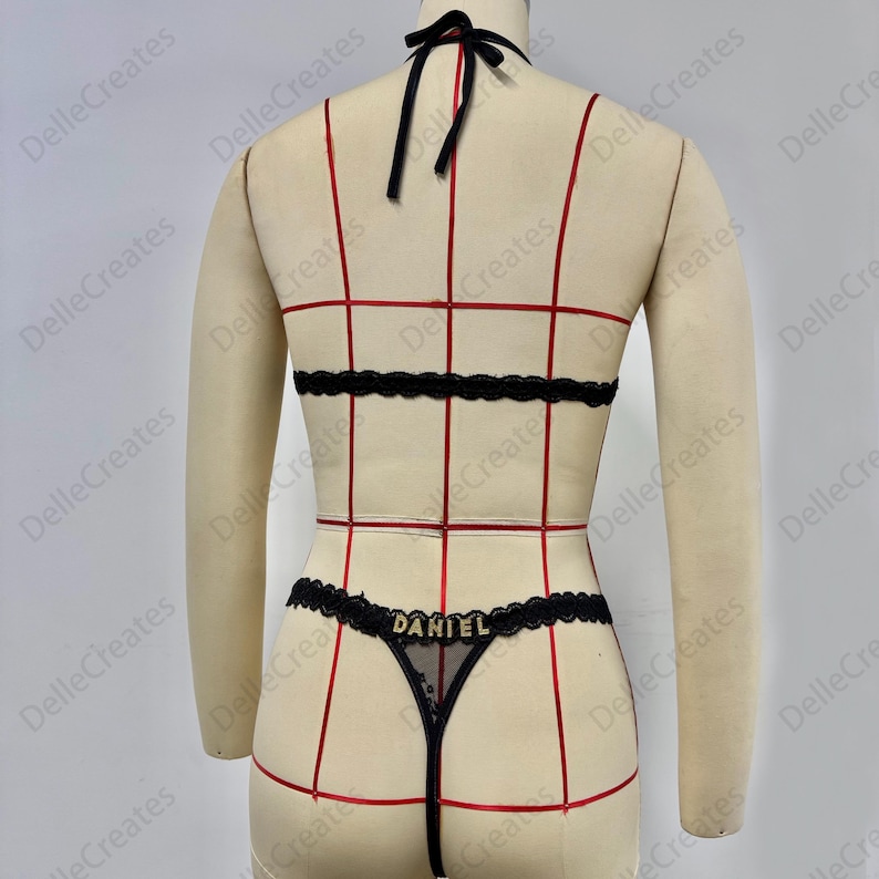Puede incluir: Conjunto de lencer&iacute;a negra con ribete de encaje y el nombre "DANIEL" en letras doradas. El conjunto incluye un top halter, una banda en la cintura y un tanga. La lencer&iacute;a se exhibe en un maniqu&iacute;.