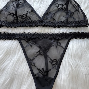 Puede incluir: Conjunto de lencer&iacute;a negra con un sujetador triangular y un tanga. El sujetador tiene delicados detalles de encaje y peque&ntilde;os lazos en las correas. El tanga tambi&eacute;n tiene detalles de encaje. El conjunto est&aacute; hecho de tela negra transparente.