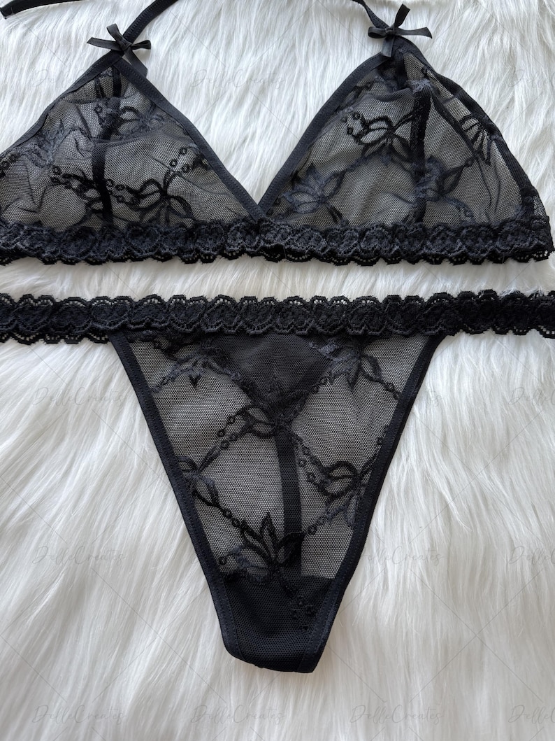 Puede incluir: Conjunto de lencer&iacute;a negra con un sujetador triangular y un tanga. El sujetador tiene delicados detalles de encaje y peque&ntilde;os lazos en las correas. El tanga tambi&eacute;n tiene detalles de encaje. El conjunto est&aacute; hecho de tela negra transparente.