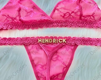 May include: Pink lace lingerie set with a matching bra and thong. The thong has the name "HENDRICK" written on the waistband.
