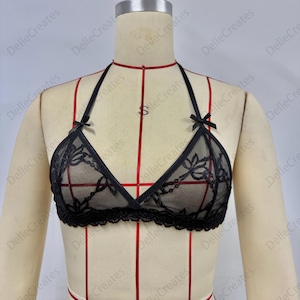 Puede incluir: Sujetador halter de encaje negro con detalles florales y peque&ntilde;os lazos. El sujetador presenta un dise&ntilde;o de copa triangular y un ribete de encaje festoneado. El sujetador se muestra en un maniqu&iacute;.