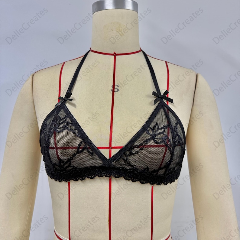 Puede incluir: Sujetador halter de encaje negro con detalles florales y peque&ntilde;os lazos. El sujetador presenta un dise&ntilde;o de copa triangular y un ribete de encaje festoneado. El sujetador se muestra en un maniqu&iacute;.