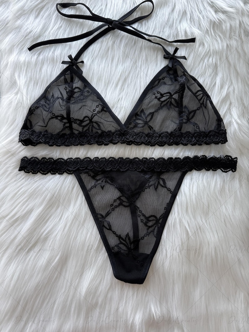 Puede incluir: Conjunto de lencer&iacute;a negra con un sujetador triangular con tirantes anudados y un tanga a juego. El conjunto est&aacute; hecho de encaje transparente con estampado floral y bordes festoneados. El sujetador tiene peque&ntilde;os lazos en los v&eacute;rtices.