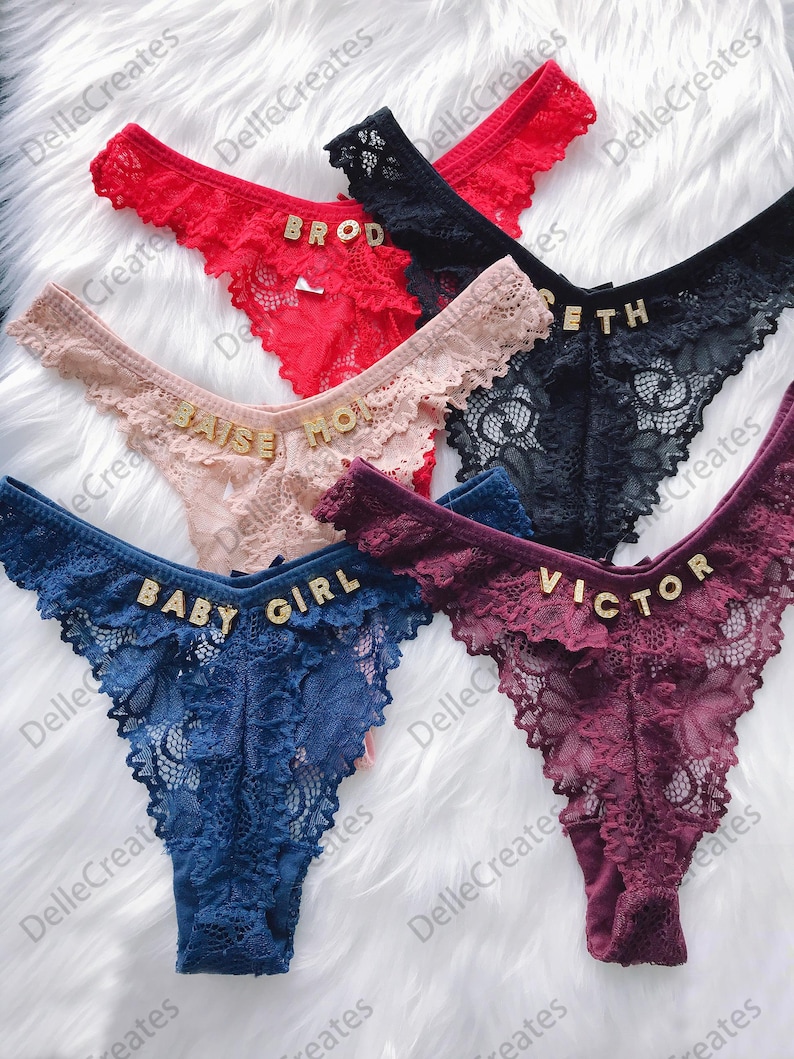 May include: Five pairs of lacy underwear with gold lettering. The lettering on the underwear reads "BROD", "BAISE MOI", "ETH", "BABY GIRL", and "VICTOR".