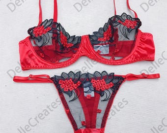 Könnte beinhalten: Rotes und schwarzes Dessous-Set mit floralen Spitzendetails. Der BH hat verstellbare Träger und einen Haken- und Ösenverschluss. Das Höschen hat einen niedrigen Bund und einen Tanga-Rücken.