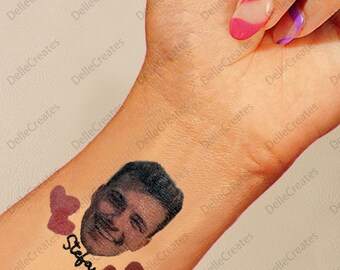 Op de afbeelding: Een tijdelijke tattoo met een portret van een man, de naam "Stefan" in cursief geschreven en twee rode harten.