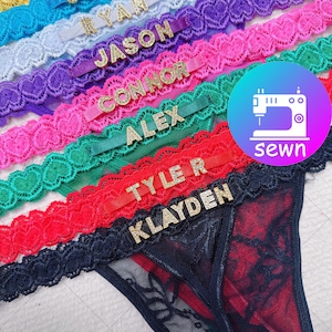 May include: A selection of colourful lace thong underwear with gold lettering spelling out names. The lace trim is in shades of blue, purple, pink, green, and red. A logo with a sewing machine and the word "sewn" is visible.