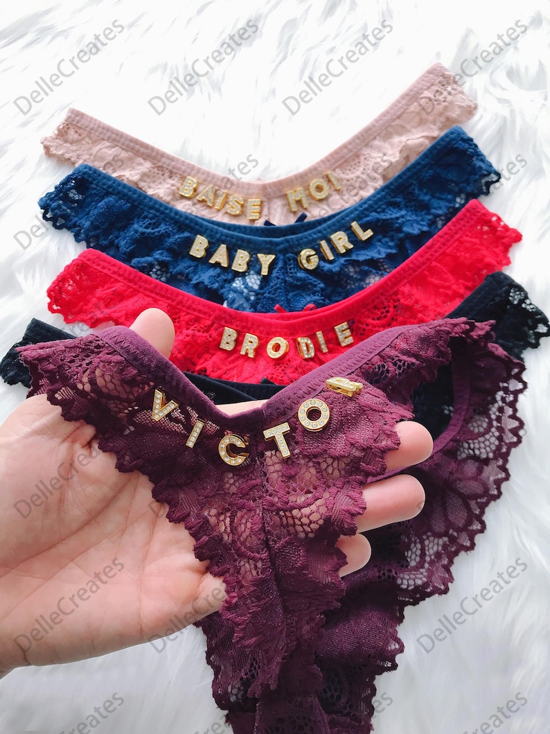 May include: Five pairs of lacy underwear with gold lettering. The lettering spells out "Raise", "Baby Girl", "Brodie", "Victor", and "Mom".