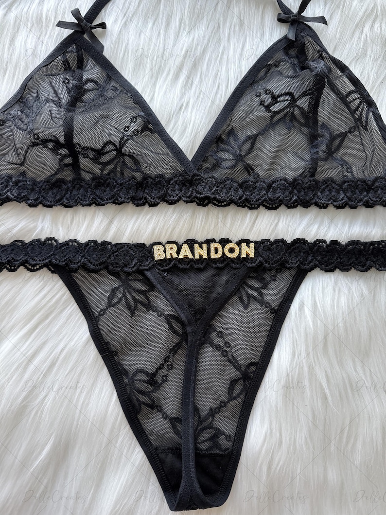 Puede incluir: Conjunto de lencer&iacute;a de encaje negro. El sujetador triangular tiene detalles de lazo, y la tanga a juego lleva el nombre "BRANDON" en letras doradas. El conjunto est&aacute; hecho de encaje transparente con estampado floral.