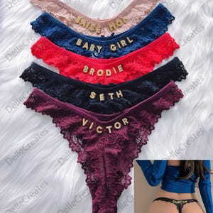 May include: A set of six lace underwear with different names embroidered on them in gold letters. The names are "Baise Mon", "Baby Girl", "Brodie", "Seth", "Victor", and "Custom".