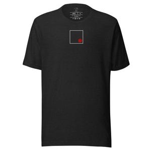 Op de afbeelding: Donkergrijze t-shirt met een minimalistisch ontwerp. Een witte vierkant met een rode stip is gecentreerd op de borst. De t-shirt heeft een ronde hals en korte mouwen. De stof lijkt een zacht, gemêleerd materiaal te zijn.
