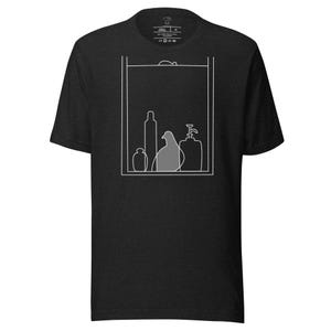 May include: Dark gray t-shirt featuring a white line drawing of a pigeon and various bottles inside a rectangular frame. The pigeon is shaded gray. The shirt has a crew neck and short sleeves.