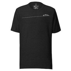 May include: Dark gray t-shirt featuring a minimalist white line drawing of a race car. The design includes a horizontal line and a small car silhouette. The shirt has a crew neck and short sleeves. Small text and symbols are printed near the collar.